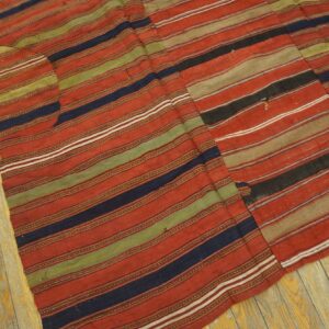 Red, navy, olive, and tan striped flatweave rug showing visible seams on worn yellow wood flooring.