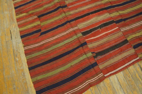 Red, navy, olive, and tan striped flatweave rug showing visible seams on worn yellow wood flooring.