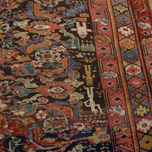 Detailed traditional rug in dark red, navy, and black with floral and geometric motifs on distressed wood floors.