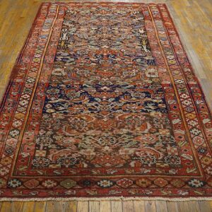 A dense patterned runner rug featuring muted red, rust, and navy tones rests on worn hardwood flooring.
