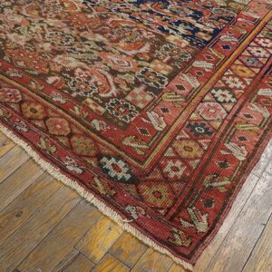 A detailed corner of a traditional red and navy patterned rug resting on light distressed wood planks.