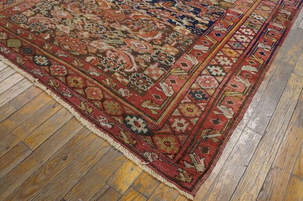 A detailed corner of a traditional red and navy patterned rug resting on light distressed wood planks.