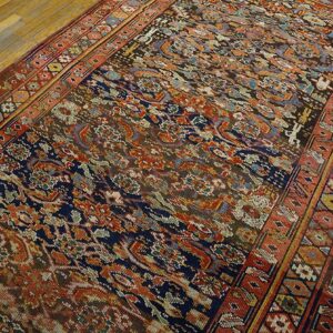 A complex patterned rug in rust, navy, brown, and light blue rests on light plank wood flooring.