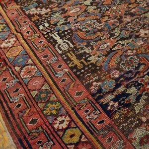 Low-pile rug detail featuring red, blue, and dark brown traditional patterns rests on light wood flooring.