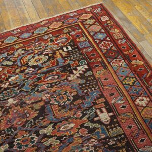 Close-up of a densely patterned rug in red, blue, and gold resting on distressed wood flooring.