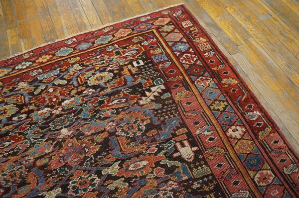 Close-up of a densely patterned rug in red, blue, and gold resting on distressed wood flooring.