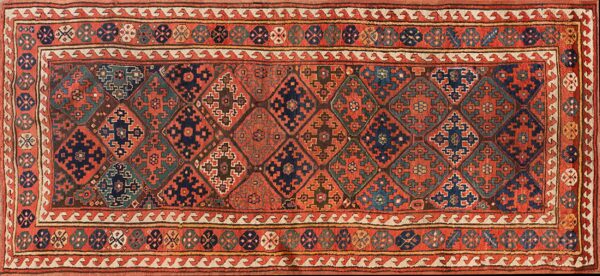 Low-pile geometric runner featuring interlocking red, navy, and teal diamond motifs and multi-layered borders.