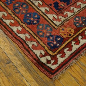 Corner of a low-pile rug with red, blue, and cream geometric patterns on distressed wood planks.
