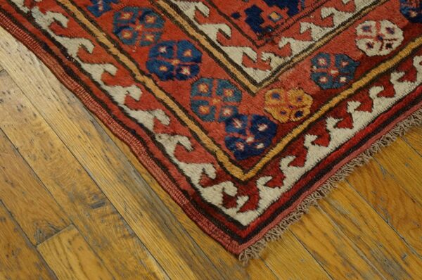 Corner of a low-pile rug with red, blue, and cream geometric patterns on distressed wood planks.