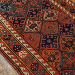 Low-pile geometric runner rug in rust, navy, and teal on distressed wood planks.