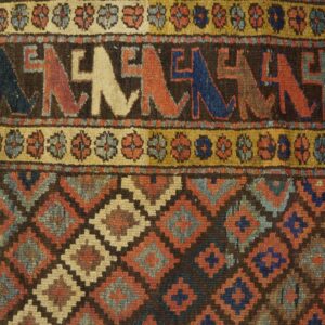 Rug detail showing geometric diamonds and stylized figures in rust, blue, and tan on wood floor.