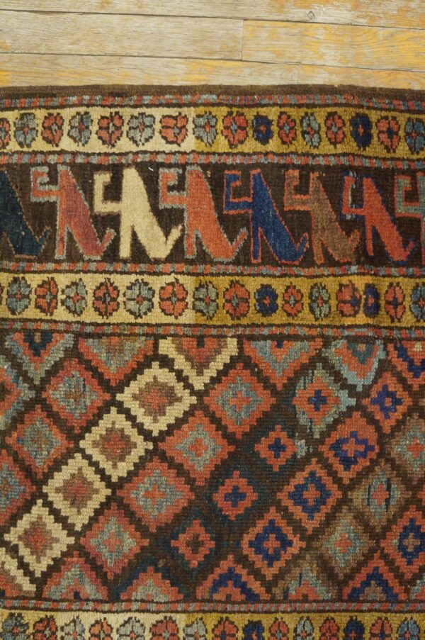 Rug detail showing geometric diamonds and stylized figures in rust, blue, and tan on wood floor.