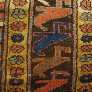 High-pile rug detail showing geometric patterns in rust, blue, and gold against light wood flooring.