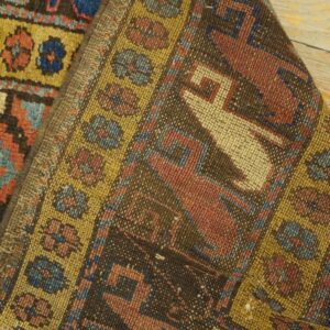 Low-pile tribal rug detail with brown, red, blue, and yellow geometric patterns folded on wood floorboards.