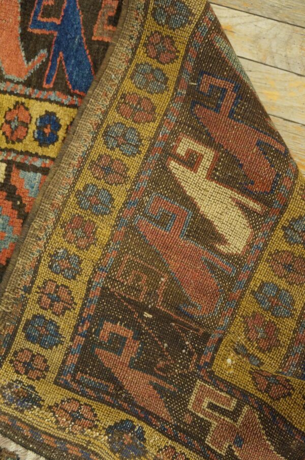 Low-pile tribal rug detail with brown, red, blue, and yellow geometric patterns folded on wood floorboards.