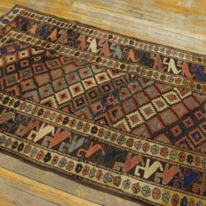 Geometric runner rug featuring stylized figures and diamonds in brown, rust, and blue, resting on worn wood floors.