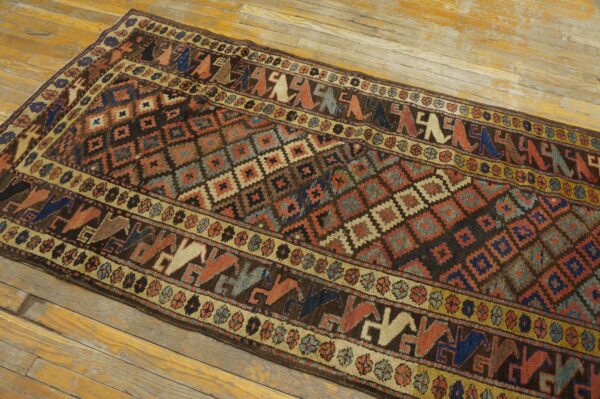 Geometric runner rug featuring stylized figures and diamonds in brown, rust, and blue, resting on worn wood floors.