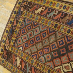 Dark brown geometric rug with rust, blue, and gold borders featuring stylized figures on distressed light wood floor.