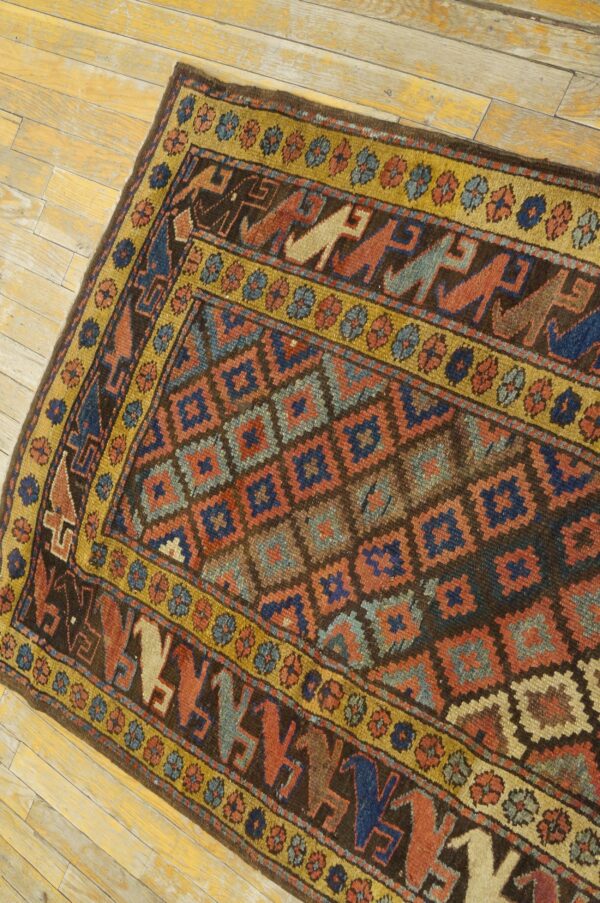 Dark brown geometric rug with rust, blue, and gold borders featuring stylized figures on distressed light wood floor.