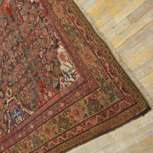 Muted red and olive traditional rug with intricate detail rests on distressed, light-colored wooden planks.