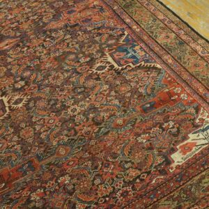 Intricate red, blue, and brown patterned rug with a multi-layered border on worn yellow wooden planks.