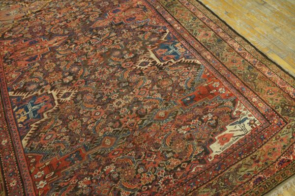 Intricate red, blue, and brown patterned rug with a multi-layered border on worn yellow wooden planks.