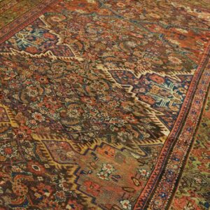 Detailed rust, blue, and green patterned rug with a wide olive border laid on pale wood flooring.