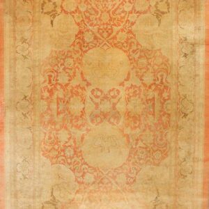 Traditional rug with a beige field and large ornate central medallion in coral and taupe.