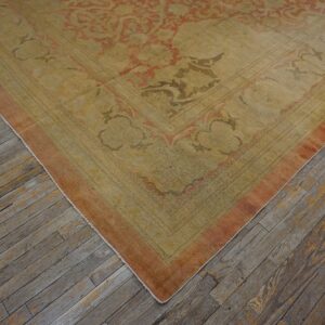 Low-pile rug with faded gold and terracotta ornate patterns rests on distressed gray wood flooring.