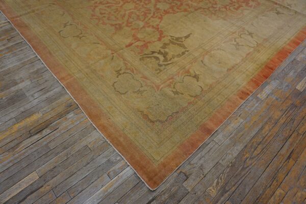 Low-pile rug with faded gold and terracotta ornate patterns rests on distressed gray wood flooring.