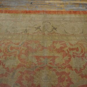 A faded low-pile rug with a coral and khaki traditional pattern rests on distressed wood plank flooring.