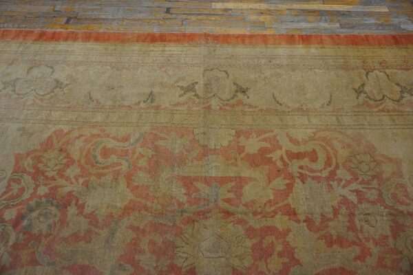 A faded low-pile rug with a coral and khaki traditional pattern rests on distressed wood plank flooring.