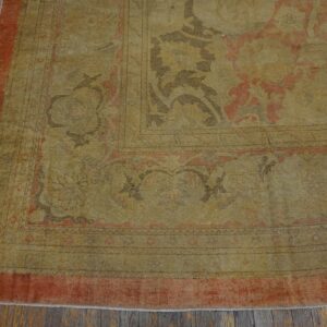 Low-pile, distressed gold and rust patterned rug detail displayed on dark, worn wood flooring.