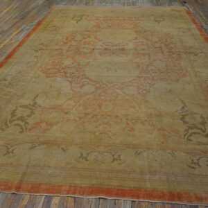 Low-pile rug with faded gold and red ornate patterns displayed on distressed wooden floorboards.