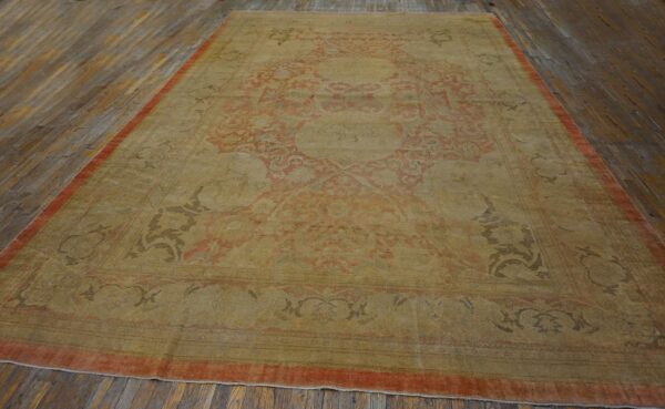 Low-pile rug with faded gold and red ornate patterns displayed on distressed wooden floorboards.