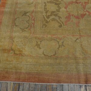 Faded low-pile traditional rug featuring gold, dusty rose, and brown accents on distressed gray wood flooring.