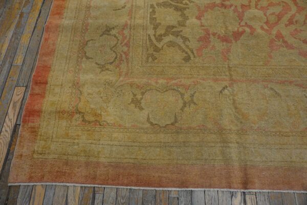Faded low-pile traditional rug featuring gold, dusty rose, and brown accents on distressed gray wood flooring.