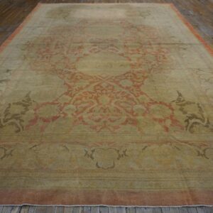 Faded low-pile rug featuring a large coral and olive medallion on dark, distressed wooden floors.