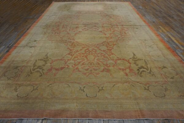 Faded low-pile rug featuring a large coral and olive medallion on dark, distressed wooden floors.
