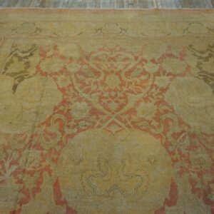 Ornate yellow and coral patterned rug with low pile on rustic wooden floorboards.