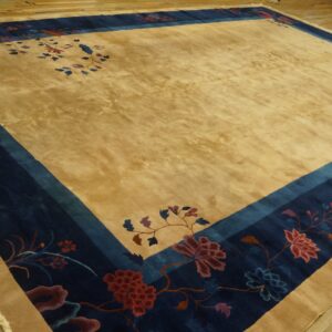 Golden field rug with a wide navy blue border and colorful floral designs on wood flooring.