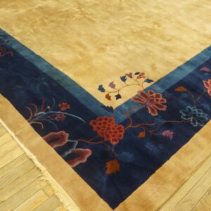 A deep pile tan rug border with navy and multicolored floral patterns rests on light wood plank flooring.