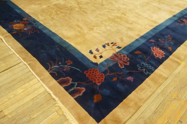 A deep pile tan rug border with navy and multicolored floral patterns rests on light wood plank flooring.