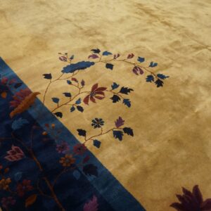 A gold rug features a stylized bird and vine pattern centered on a dark blue diagonal border.