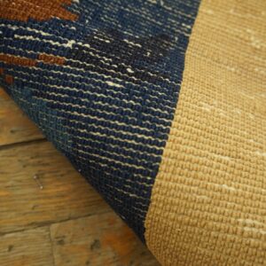 Detail shot of a rug folded over, revealing the textured tan back and the navy and brown patterned front.