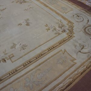 Cream rug featuring classical brown and mauve floral motifs and an architectural border on dark wood.