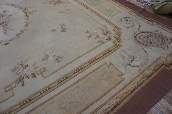Cream rug featuring classical brown and mauve floral motifs and an architectural border on dark wood.