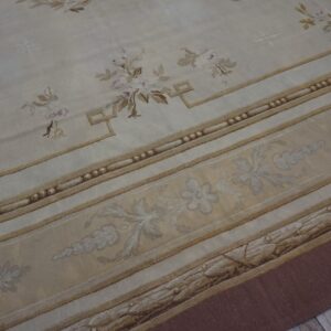 Ornate cream and gold low-pile rug featuring scattered floral sprigs and complex architectural borders on wood flooring.