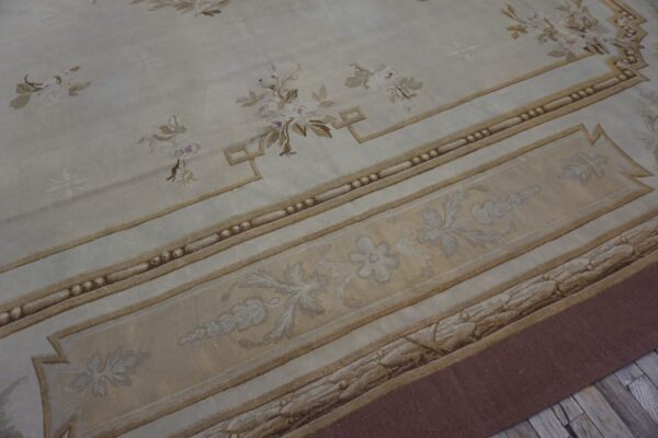 Ornate cream and gold low-pile rug featuring scattered floral sprigs and complex architectural borders on wood flooring.