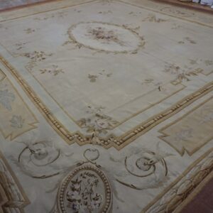 Large neoclassical rug with light floral designs, detailed borders, and a maroon outer edge on wood planks.